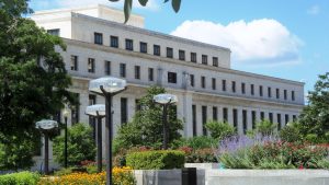The Eccles Building, headquarters of the Federal Reserve Board in Washington, DC, seen behind trees and flower beds.