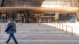 The glass-fronted entrance of JPMorgan Chase's headquarters at 270 Park Avenue in New York, with wide stone steps and a pedestrian walking past.