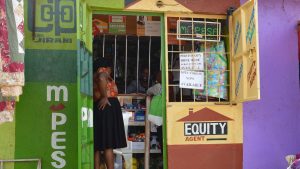A green M-Pesa mobile money kiosk beside an Equity Bank agent counter in Nairobi, with a customer standing at the window.