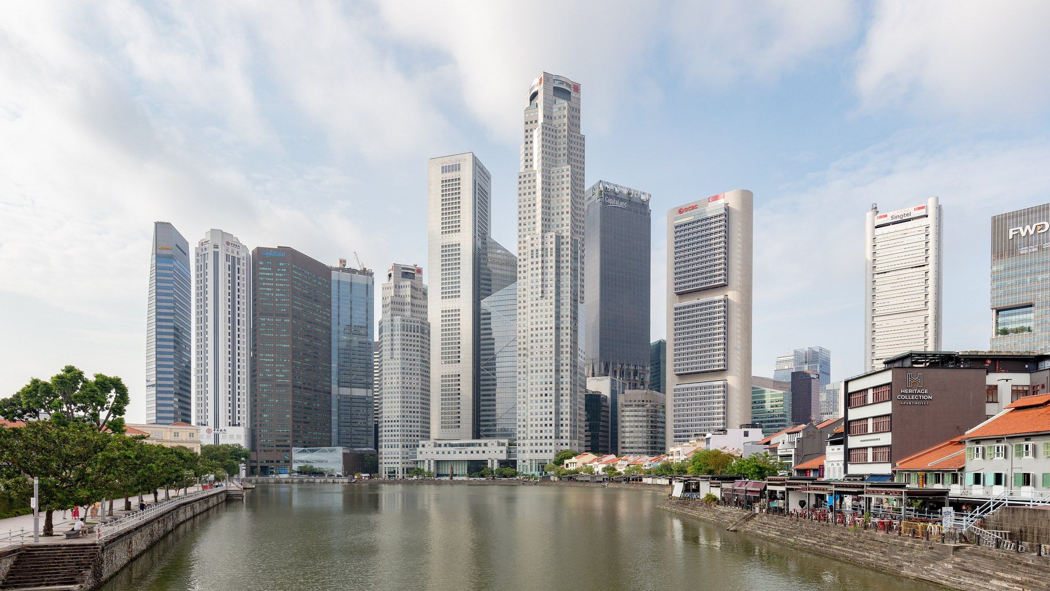 Singapore's Raffles Place financial district skyline seen across the Singapore River from Boat Quay, with shophouses on the right bank.